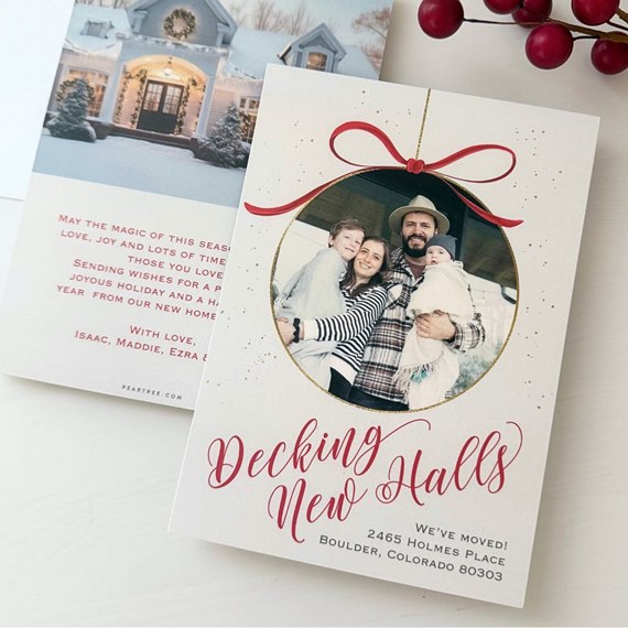 Holiday photo card with family portrait in ornament frame, red bow, gold border and red script headline