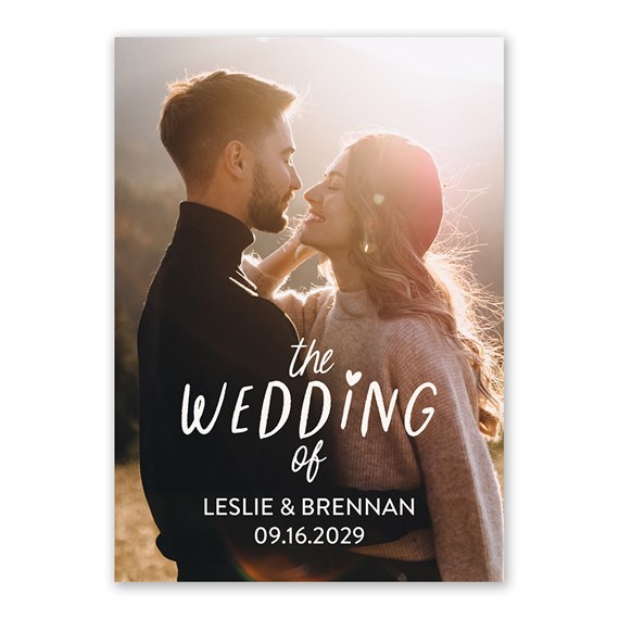 Wedding invitation card featuring a photographed couple embracing at sunset with large handwritten-style title text and placeholder for names and date.