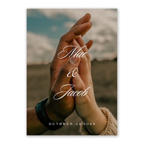 Invitation photo with two hands held together over a field, elegant script text centered and a date printed at the bottom.