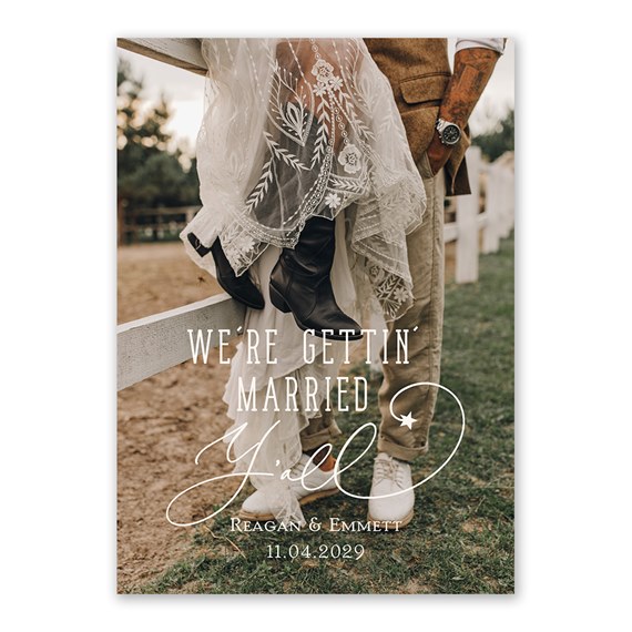 Rustic wedding invitation showing bride's lace dress and black cowboy boots with groom in tan pants and white sneakers by a white fence, white script text with wedding date.