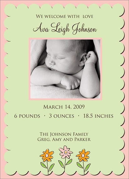 Birth announcement card with scalloped green panel and pink border, black-and-white baby photo at center, brown serif text showing birth details, and three small flower illustrations at the bottom