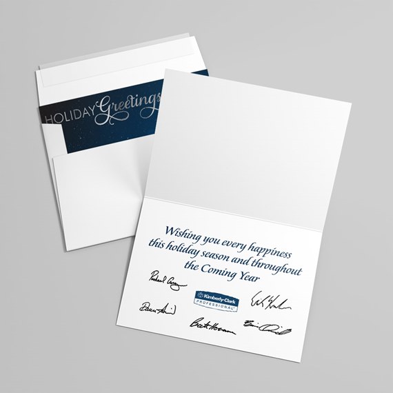 Folded holiday greeting card with navy inner panel, printed seasonal message and multiple signatures, shown with white envelope