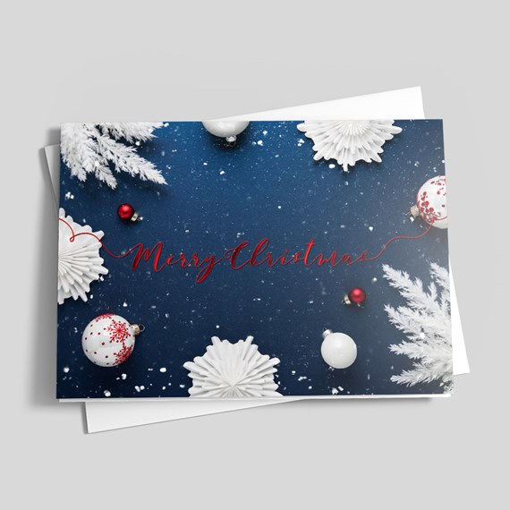 Folded Christmas card with navy blue snowy background, white paper snowflakes and frosted branches, red 'Merry Christmas' script and red and white bauble ornaments.
