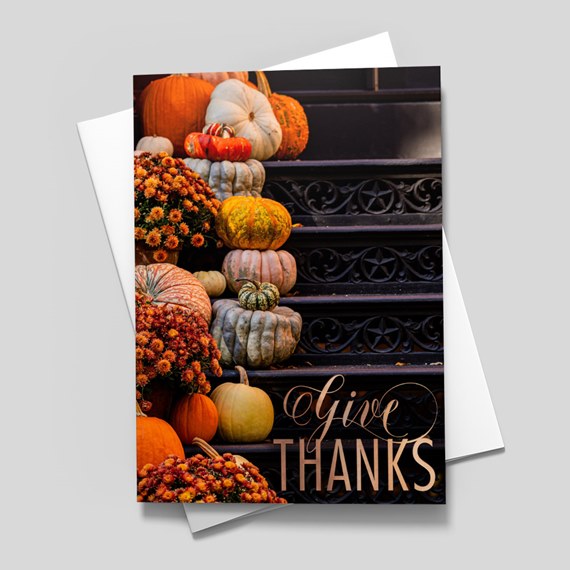 Card with stacked pumpkins and orange mums on dark decorative steps reading "Give Thanks"