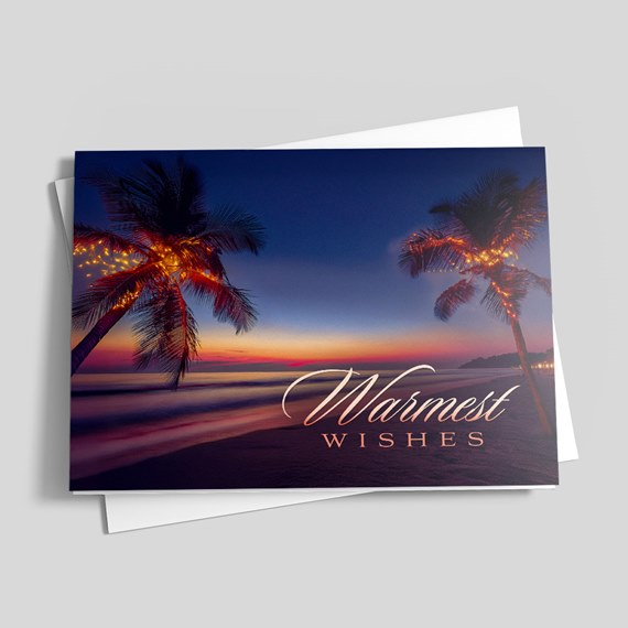 Folded greeting card showing a sunset beach with palm trees wrapped in string lights and the text 'Warmest Wishes'.