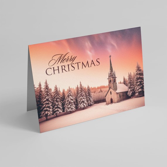 Folded Christmas card with snowy pine forest, small wooden church, pink-orange sunset sky and 'Merry Christmas' text.