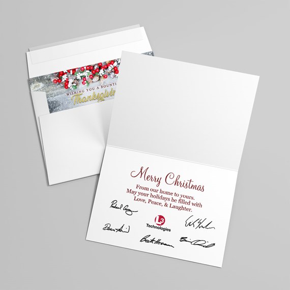 Folded Christmas greeting card with red greeting, printed signatures and logo, next to an envelope with berry and pine cone liner