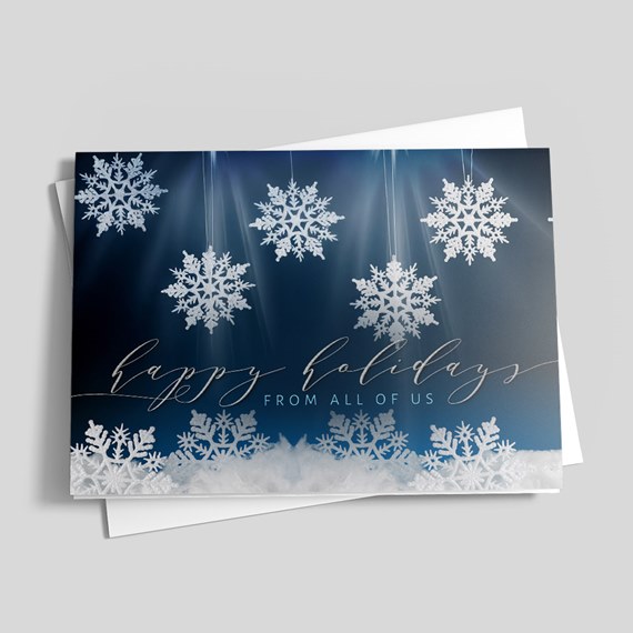 Folded holiday greeting card with white snowflakes on a navy blue background and scripted holiday message, shown with white envelope