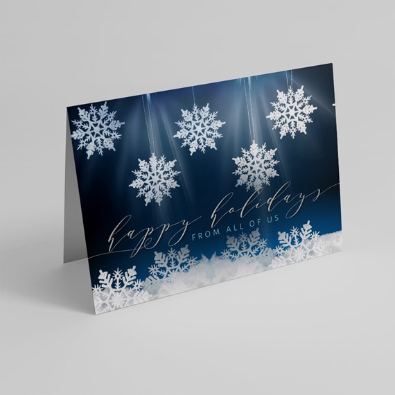Folded holiday greeting card with white snowflakes on a navy blue background and cursive holiday text