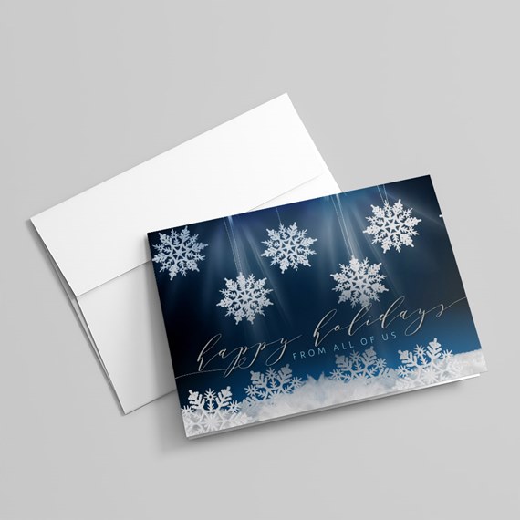 folded holiday greeting card with navy background, hanging white snowflakes and scripted "happy holidays" text, shown with white envelope