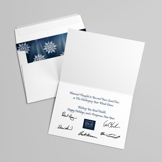 White folded holiday card with blue text and signatures, paired with envelope showing navy snowflake liner