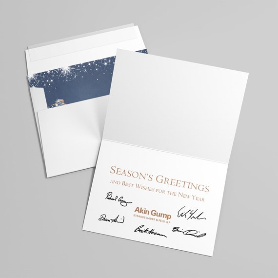 Folded white holiday card with gold "Season's Greetings" text, printed signatures, and a navy starburst envelope liner