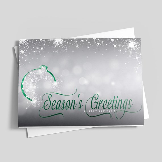 Holiday greeting card with green "Season's Greetings" script on a silver-gray background, white star sparkles and ornament graphic, shown with envelope