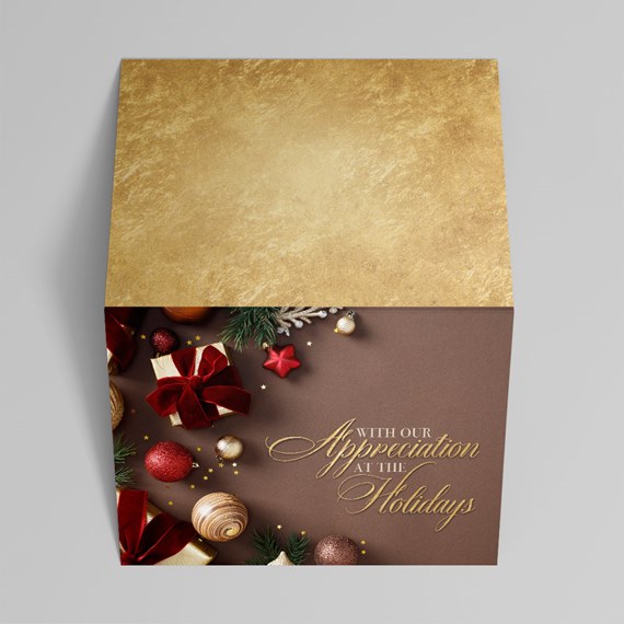 Square holiday gift box with gold lid, brown base, red bows, ornaments and gold script message