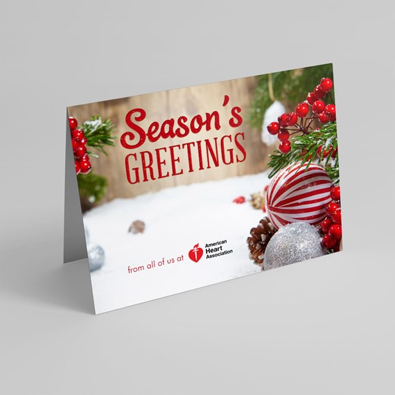 Folded holiday greeting card reading "Season's Greetings" with red striped ornament, silver bauble, pine branches and red berries