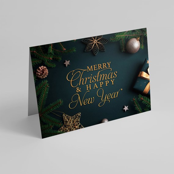 Folded Christmas greeting card with dark green background and gold script 'Merry Christmas & Happy New Year', decorated with pine branches, ornaments and a gift.