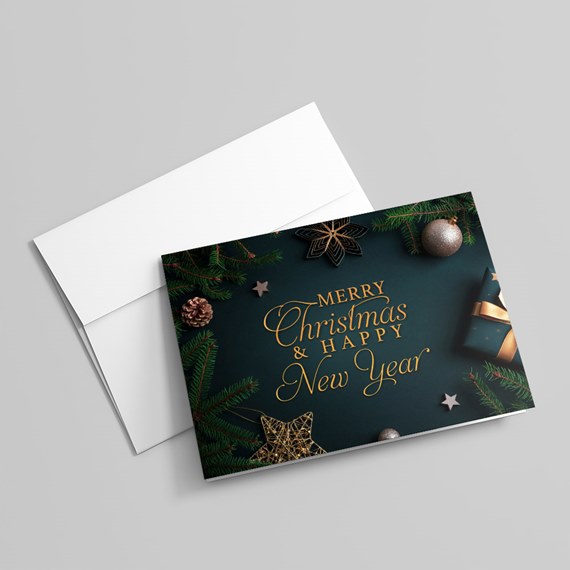 Dark green Christmas greeting card with gold 'Merry Christmas & Happy New Year' text, pine branches, ornaments and gift, shown with a white envelope