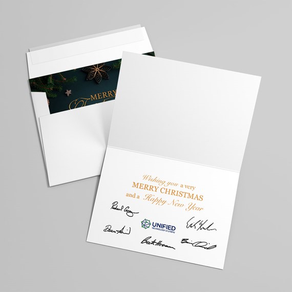 Open folded holiday greeting card with printed seasonal message and signatures, accompanied by an envelope with a dark festive liner