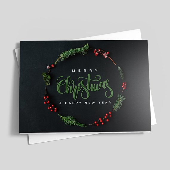 Folded black Christmas card with green script 'Christmas', white 'Merry' and '& Happy New Year', decorated with pine sprigs and red berries in a wreath.