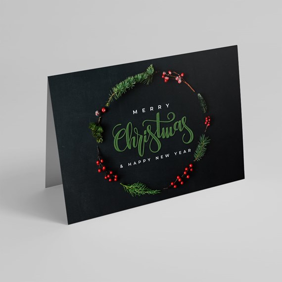 Black folded Christmas card with pine wreath, red berries, green script and white greeting text