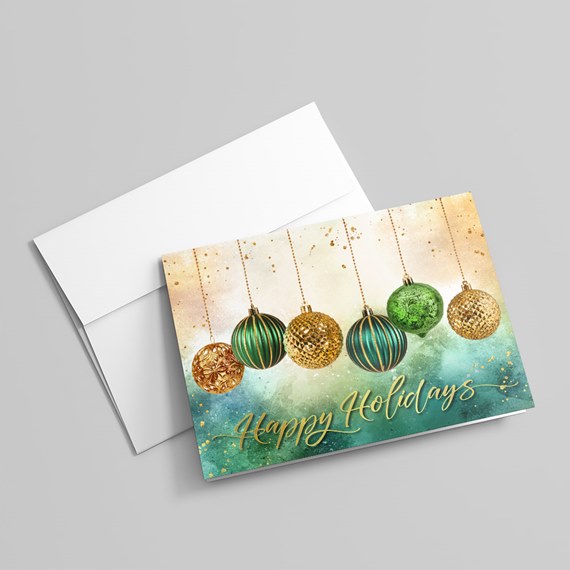 Folded holiday greeting card with green and gold hanging ornaments and teal watercolor background shown with a white envelope