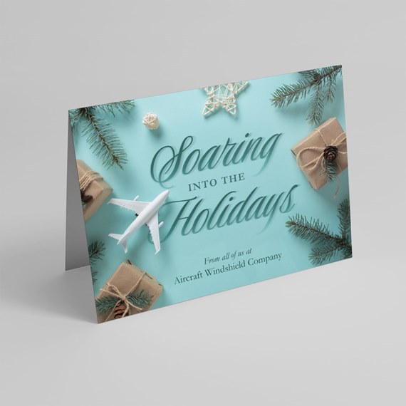 folded teal holiday greeting card with a white airplane, pine branches, kraft-wrapped gifts and a star ornament