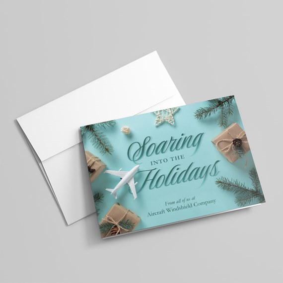 Teal holiday card with white airplane, kraft-wrapped gifts, pine sprigs, decorative star, and cursive holiday message