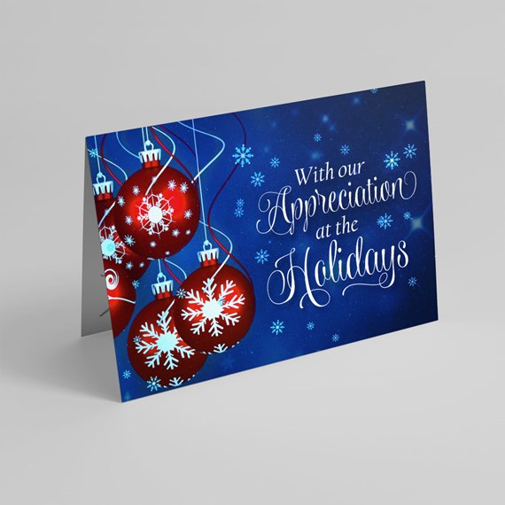 Folded holiday greeting card with red ornament baubles and white snowflakes on a blue background and white script text.