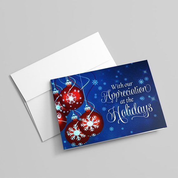 Holiday greeting card with blue background, red ornaments adorned with white snowflakes and white script text, shown with a white envelope.
