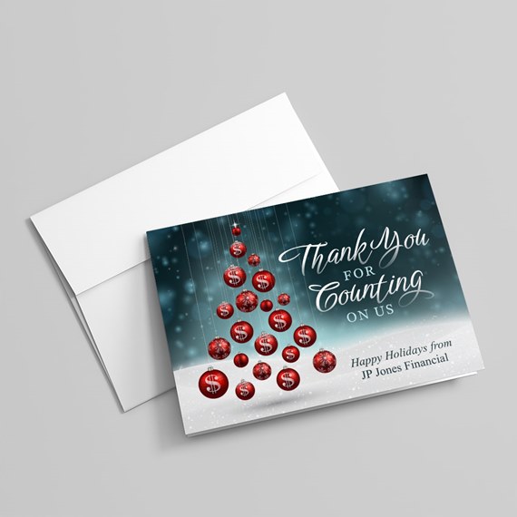 Folded holiday thank-you card with red hanging ornaments forming a tree on a teal bokeh background and white envelope