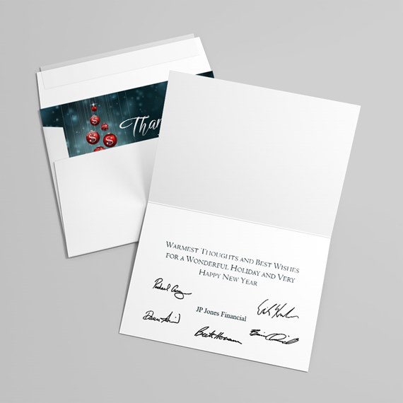 Folded holiday greeting card and envelope with printed message, signatures, and a teal insert featuring red ornaments