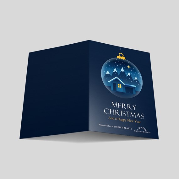 Folded navy blue Christmas card with hanging ornament illustration of a snowy house and mountains