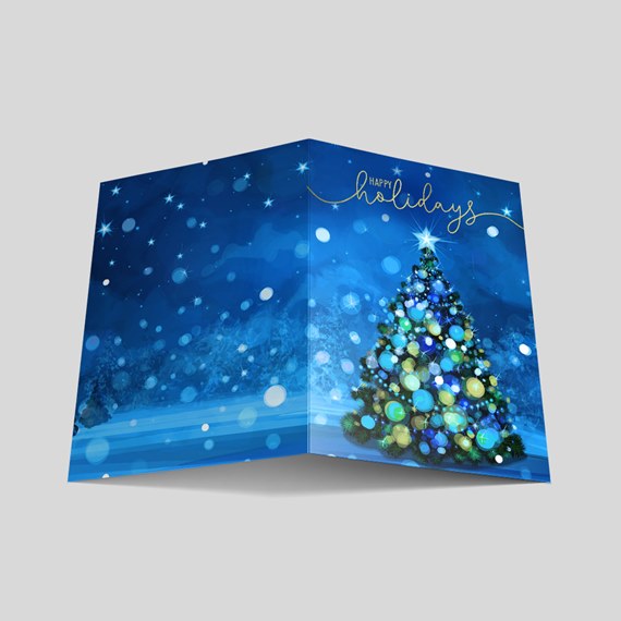 Folded holiday greeting card with decorated Christmas tree and gold "Happy Holidays" script on blue starry background