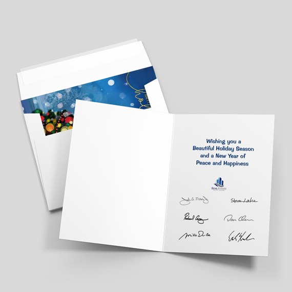 Folded holiday greeting card with printed seasonal message and blank left panel, shown with a white envelope with blue festive liner.