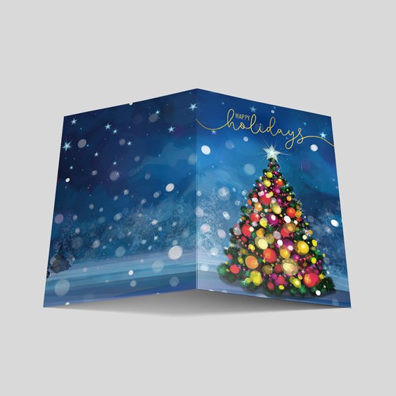 Folded holiday greeting card with decorated christmas tree, multicolored ornaments, snowy blue night scene and gold 'Happy Holidays' script