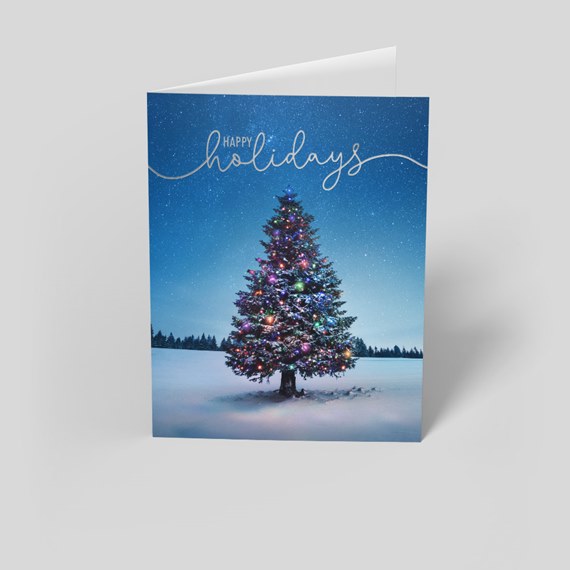 Folded holiday card with a lit Christmas tree adorned with colorful lights standing in snow beneath a starry blue sky and 'Happy Holidays' script