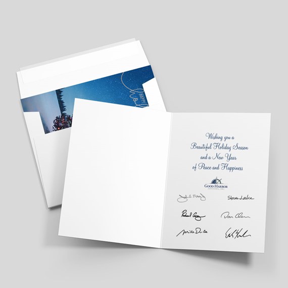 Folded holiday greeting card open to show printed message and signatures, paired with envelope featuring a blue starry liner and Christmas tree detail.