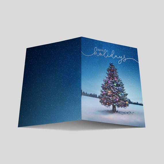 Folded holiday greeting card with decorated Christmas tree in snow, starry blue sky and gold "Happy holidays" script