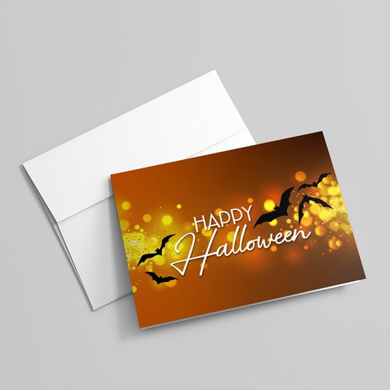 Orange Halloween greeting card with yellow bokeh, black bats and white 'Happy Halloween' script with white envelope.