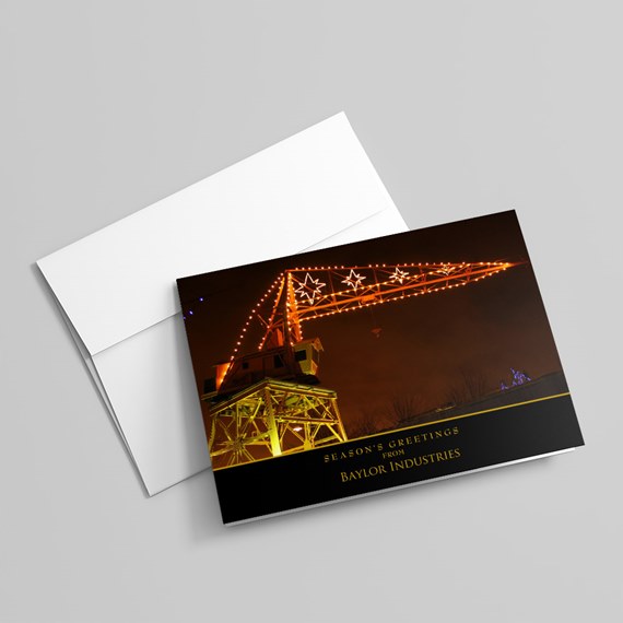 Folded greeting card showing an illuminated industrial crane with star-shaped string lights at night, shown with a white envelope