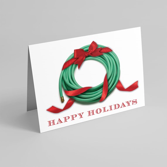 Folded holiday greeting card featuring a green garden hose shaped into a wreath with red ribbon and 'Happy Holidays' text.