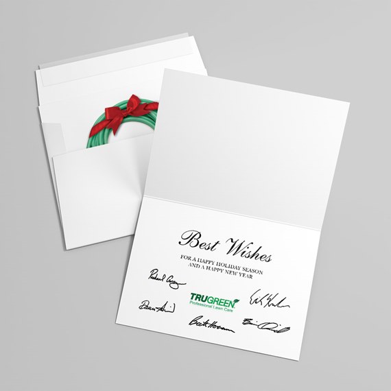 Folded white holiday card with wreath and red bow in envelope, "Best Wishes" printed message and signatures