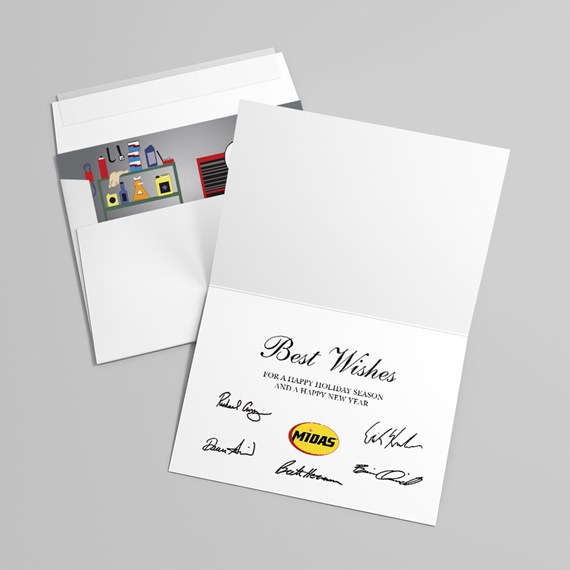 Folded white greeting card with printed greeting and signatures, small yellow circular logo, and envelope with illustrated workshop liner