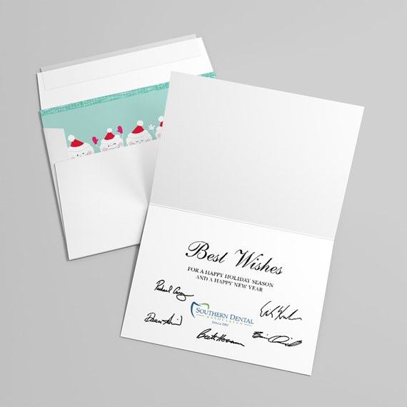Folded white holiday greeting card with 'Best Wishes' text and signatures, paired with an envelope featuring a teal liner decorated with Santa faces in red hats.