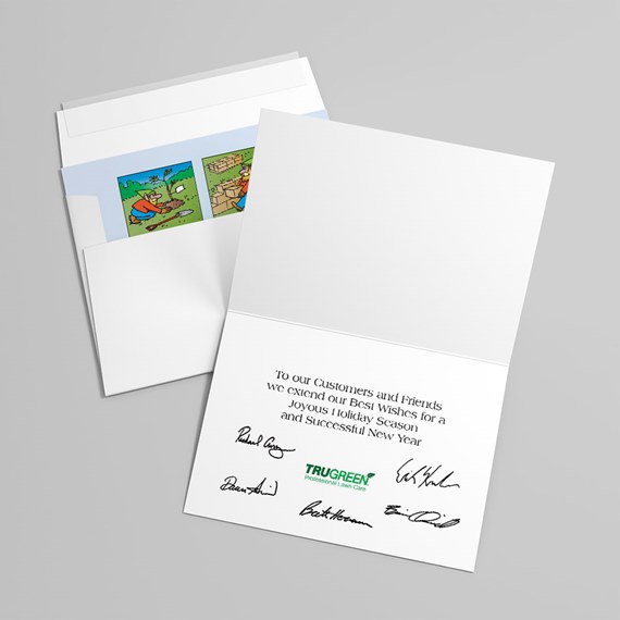 Open folded holiday greeting card with printed message, signatures and green logo, next to an envelope with a colorful illustrated insert