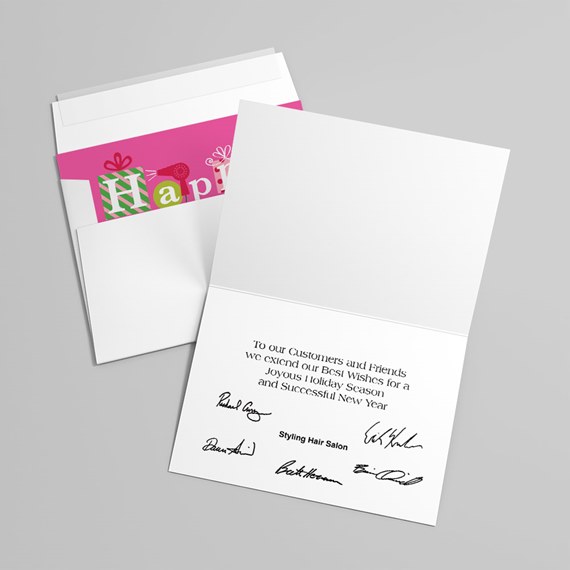 Folded white holiday greeting card with printed message and signatures, paired with envelope showing pink and green holiday liner