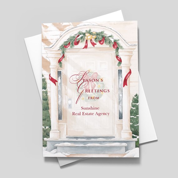 Holiday greeting card showing a painted front door with garland, red ribbons, snowy steps and a printed seasonal greeting