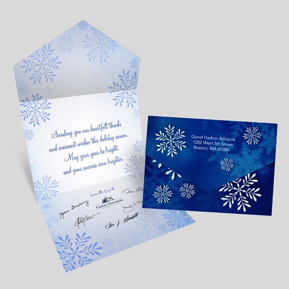 folded holiday card with blue snowflakes and matching dark blue envelope showing printed address